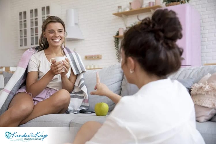 Two women talking on a couch, sharing support during recovery at a treatment center.